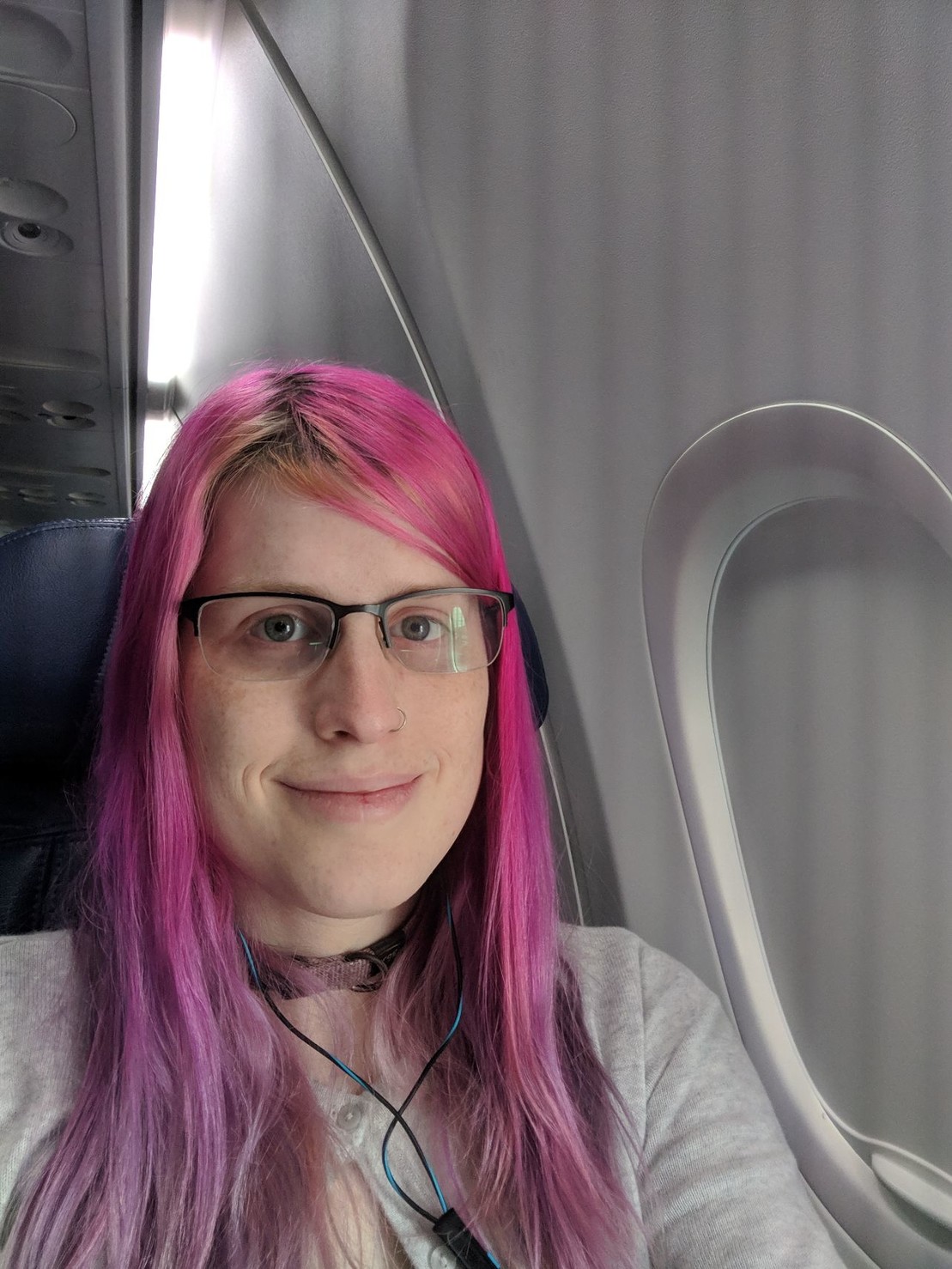 a smiling pink haired woman on an airplane