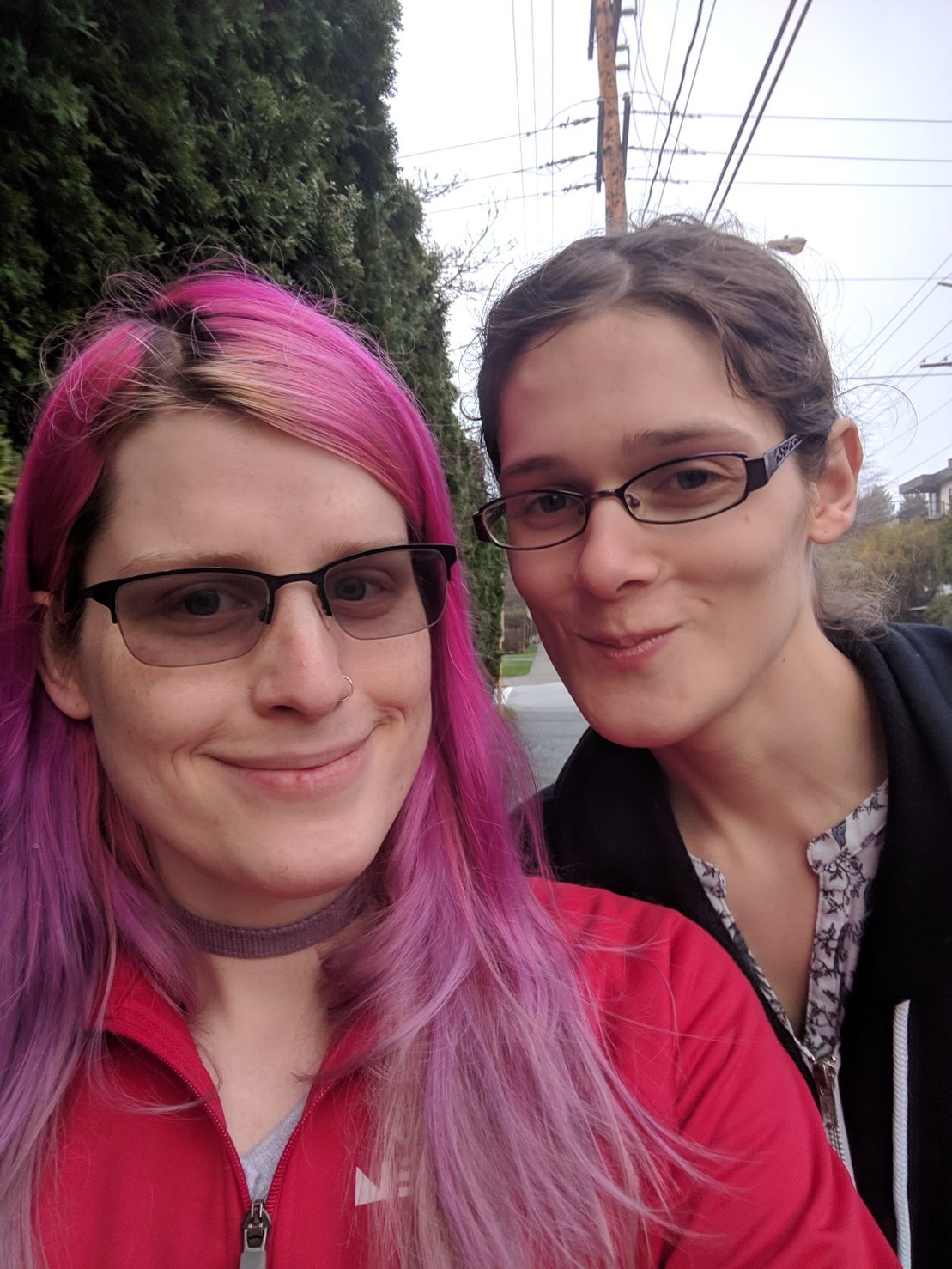two smiling women on a pavement, one with pink hair the other a brunette