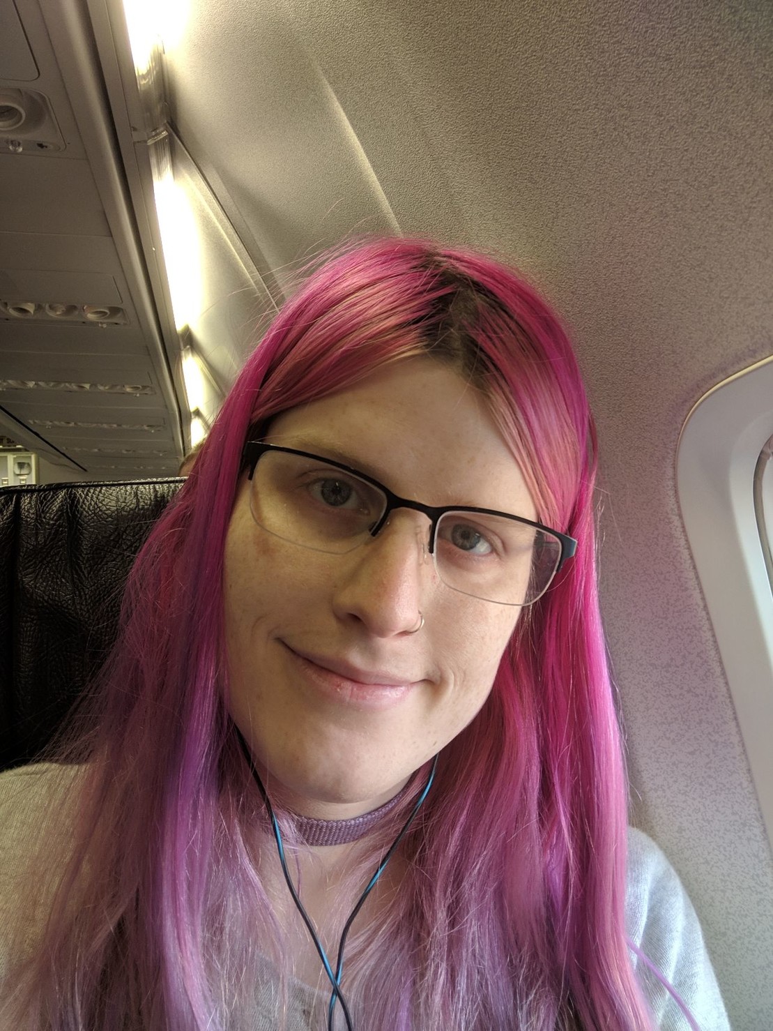 a tired but smiling pink haired girl on a plane