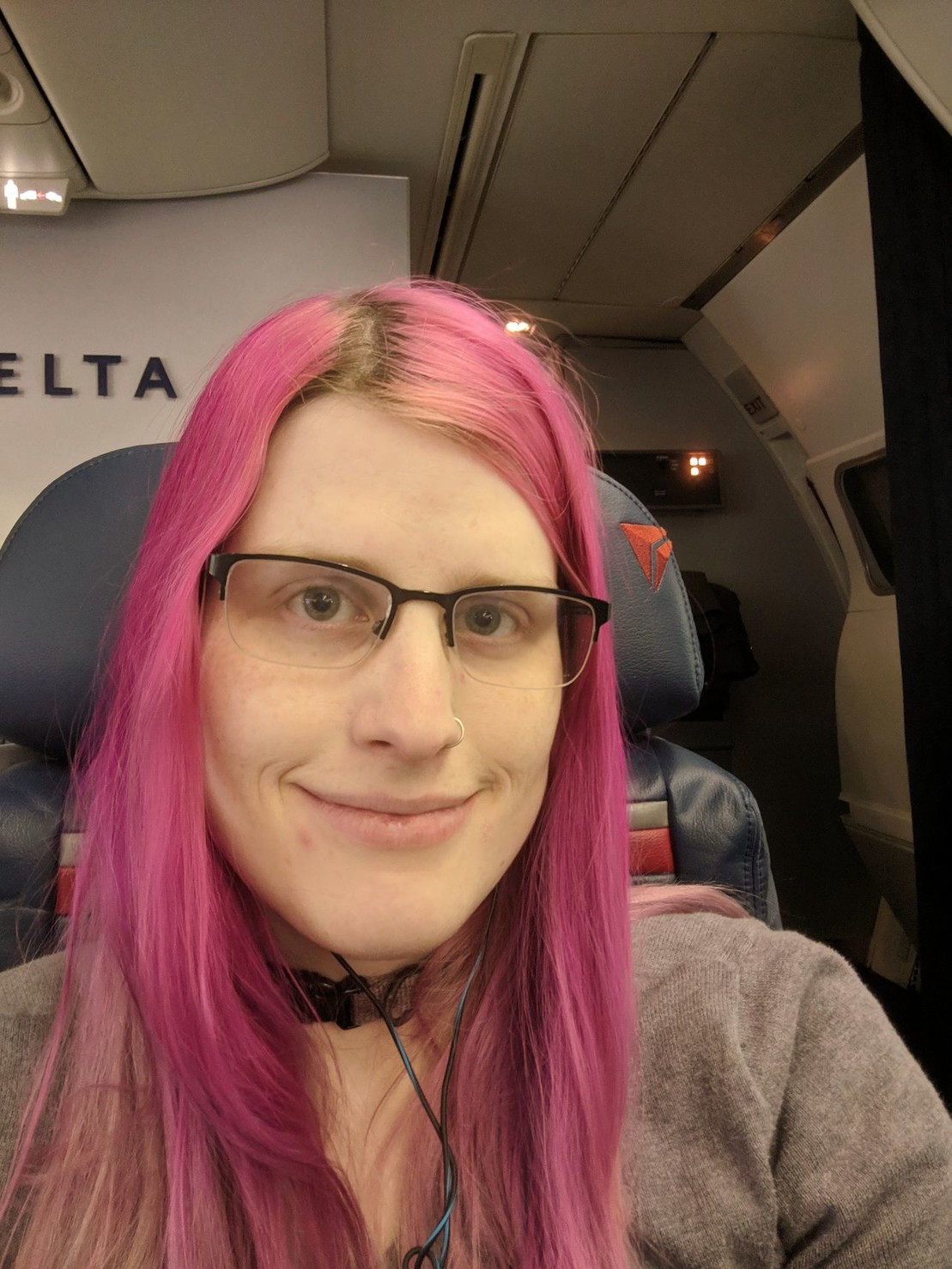 a smiling pink haired woman in first class on a plane