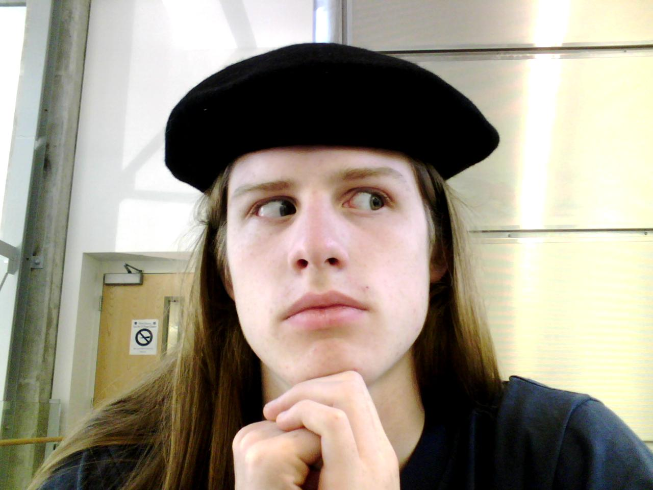 A weird maybe-boy looking to the side. They have long blonde hair and are wearing a beret.