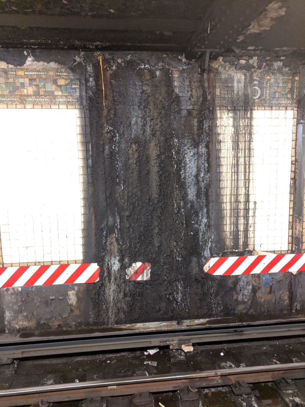 a subway wall covered black corrosion and water stains. the red safety markers are completely obscured