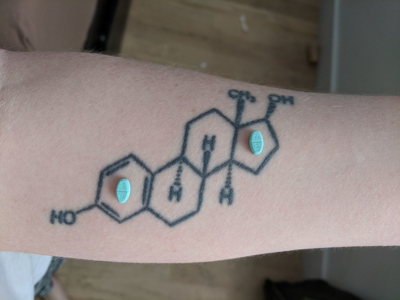 two oestrogen pills resting on the oestrogen molecule tattoo on my arm