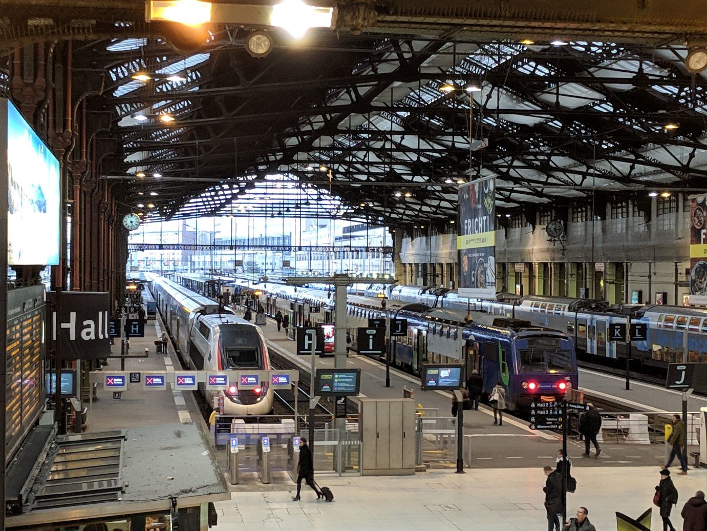 a large trai shed awning over a huge atrium. multiple trains are visible on even more tracks. both sleek high speed trains and boxy local trains are visible