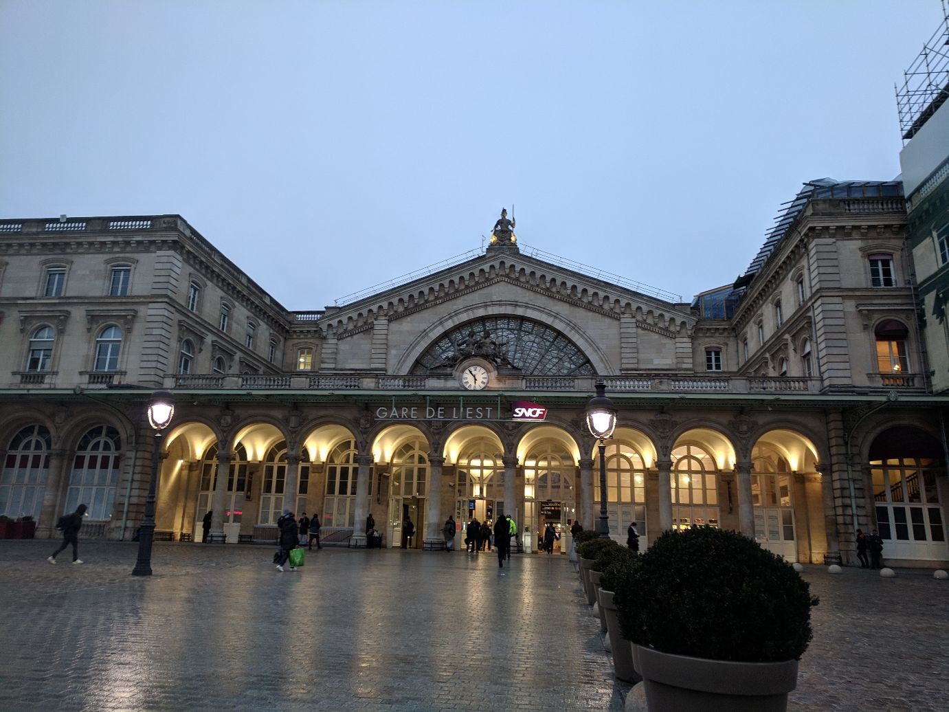 a large half-circular window above a series of archways. a clock is centered above GARE DE L'EST in large letters