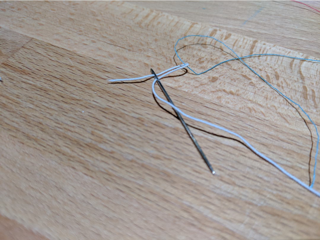 using a small piece of thread to pull elastic thread through a needle