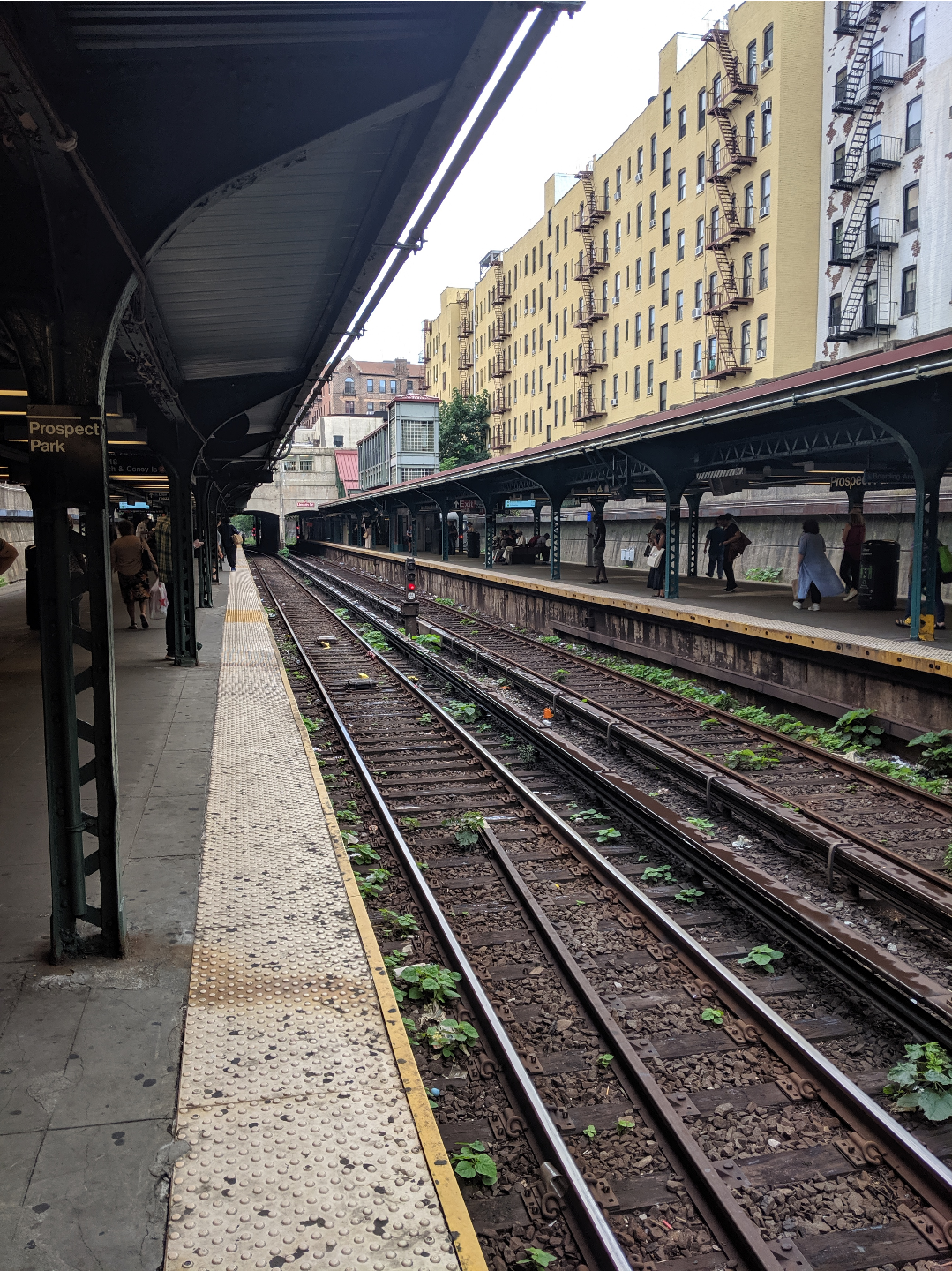 an outdoor train station with two island platforms. a block of apartments is visible above the right side