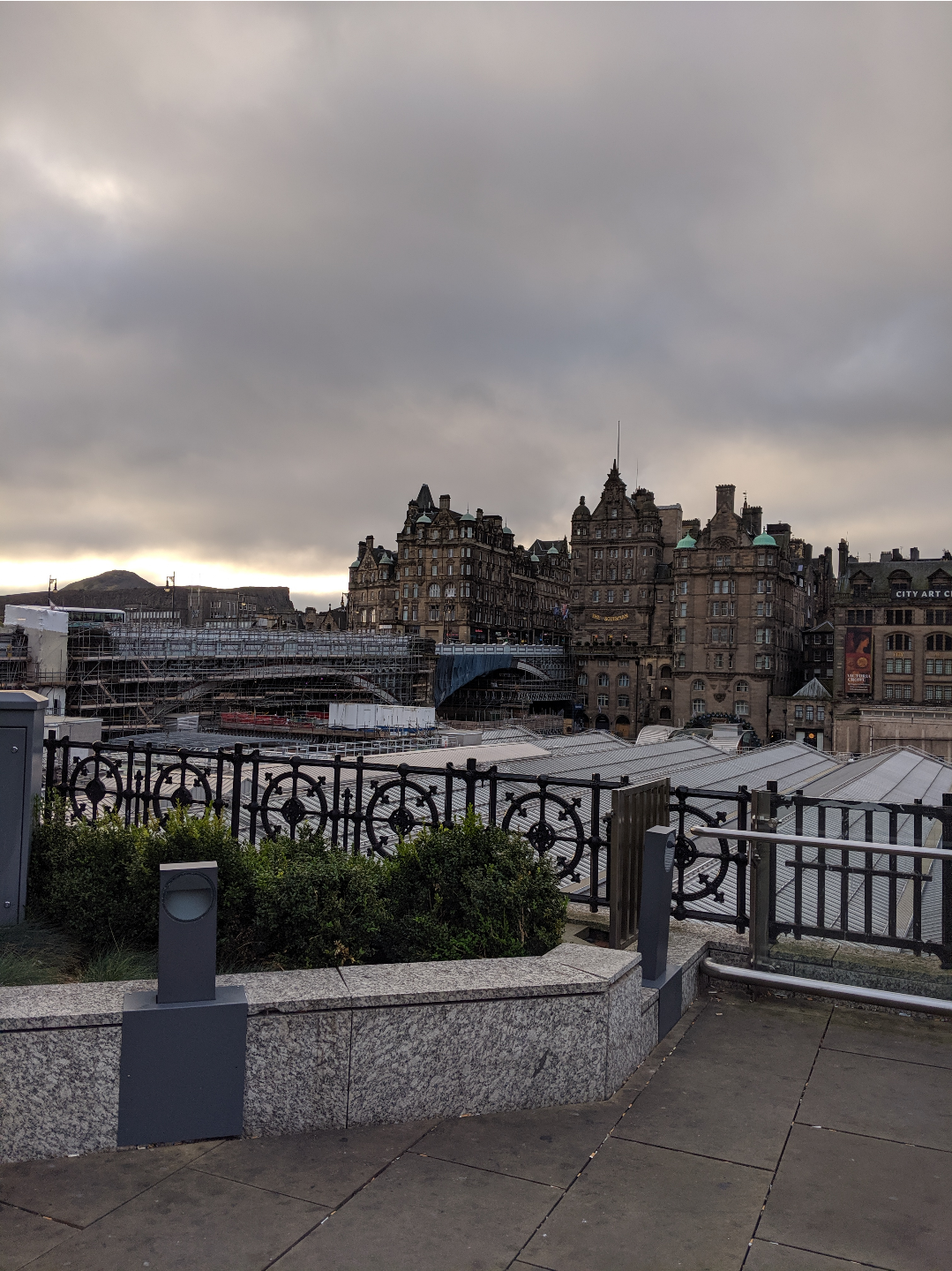 a bunch of ancient looking ornate stone buildings, across the glass roof of a train shed