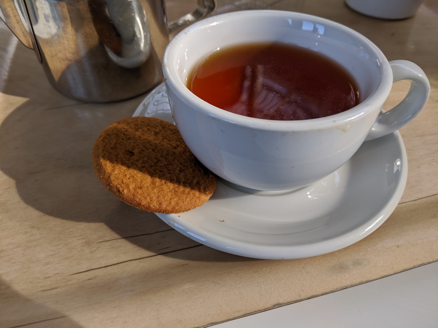 a mug of deep red tea and a single biscuit on a tray
