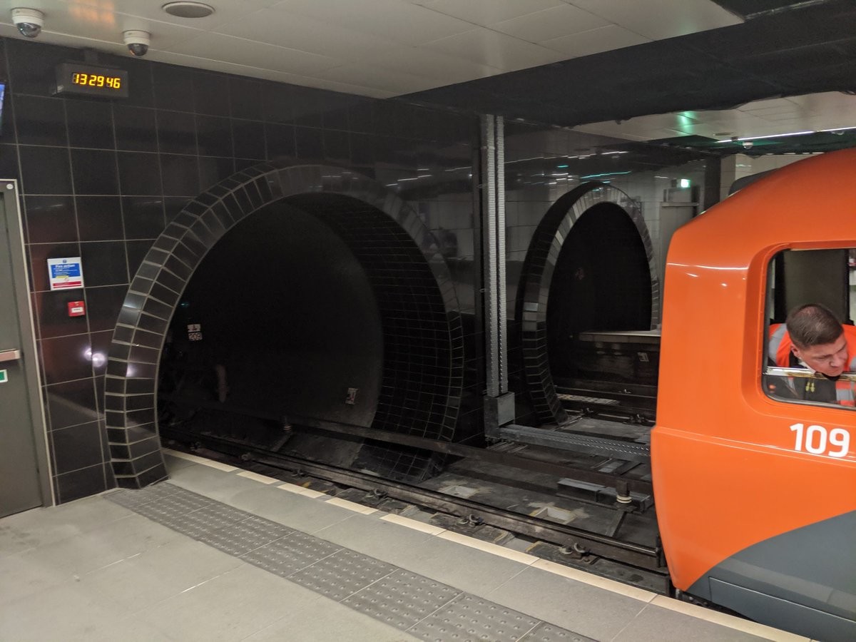 A driver sticks his head out as an orange subway prepares to enter a tunnel