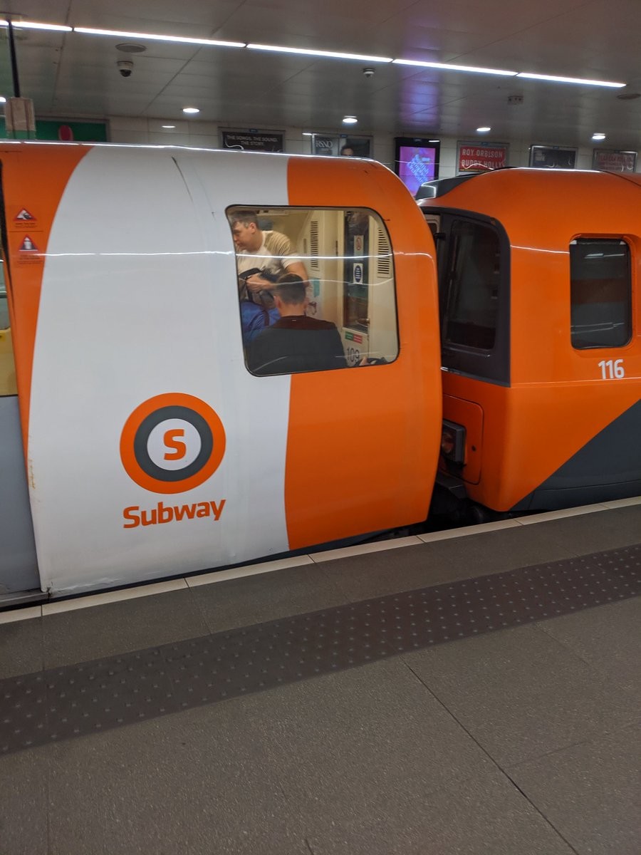 Two small orange trains, one bearing a logo of  orange and grey concentric circles with an orange S in the middle