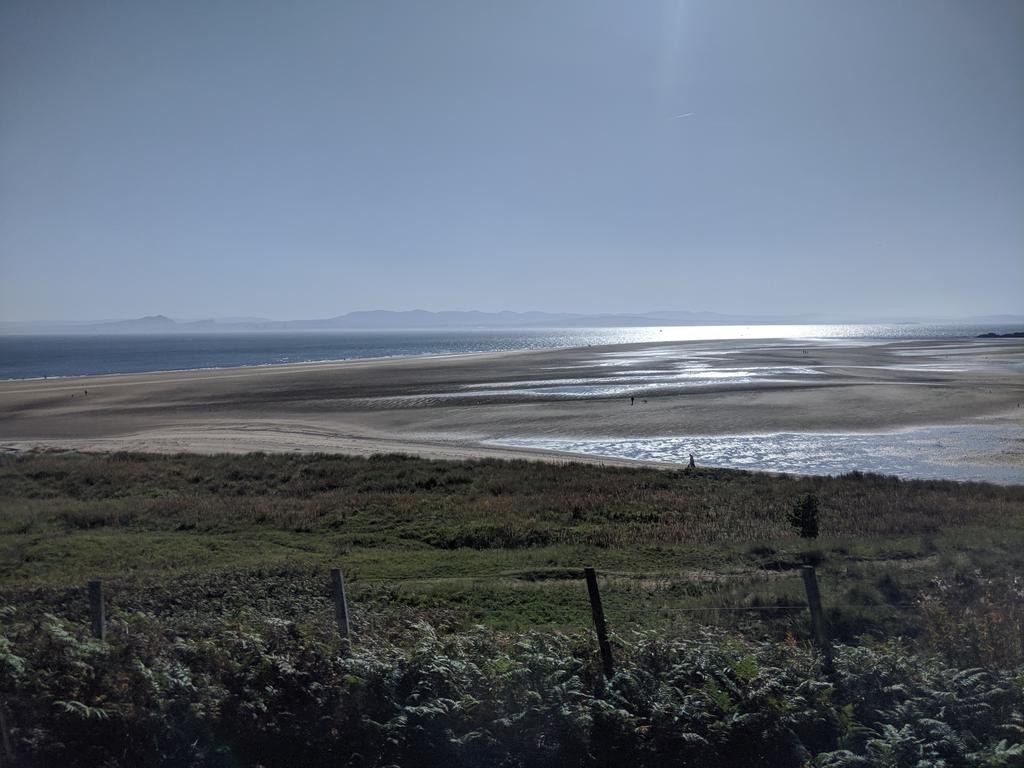 A partially submerged beach shining in the sun. Across the bay the shape of mountains can just be made out