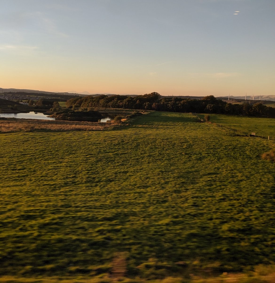 A green field, a reservoir, and a forest