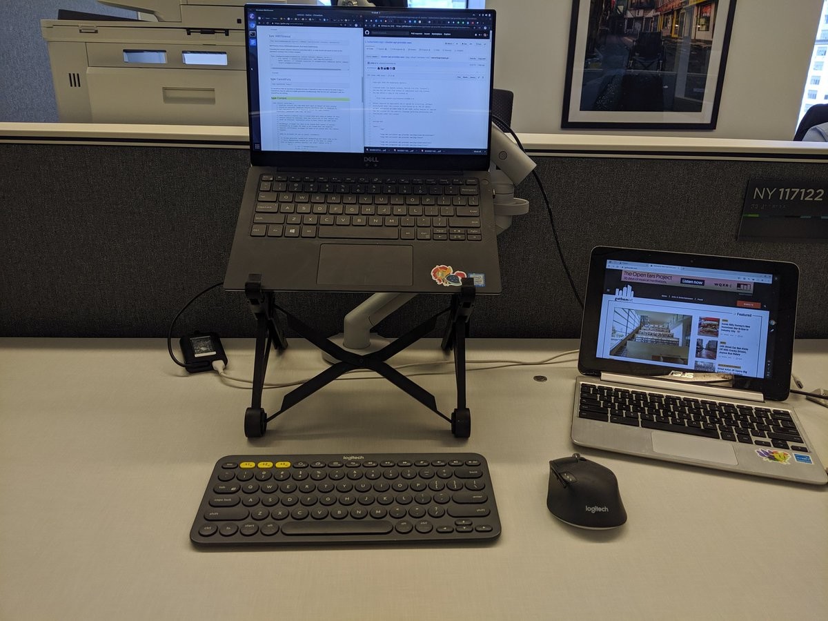 A laptop on a stand, an external keyboard and mouse, and a smaller laptop off to the side