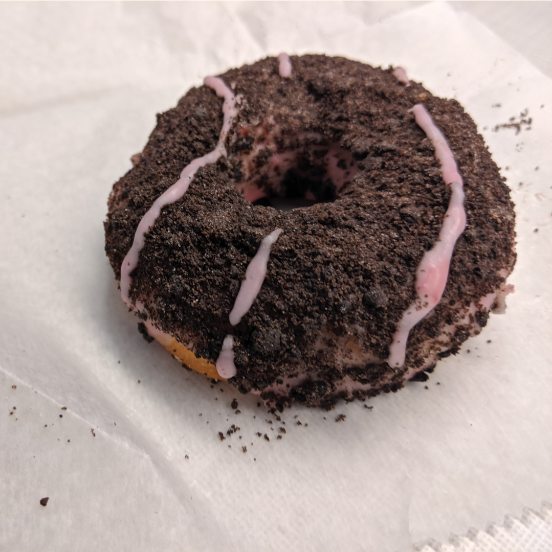 a raised doughnut covered in Oreo crumbs and raspberry frosting