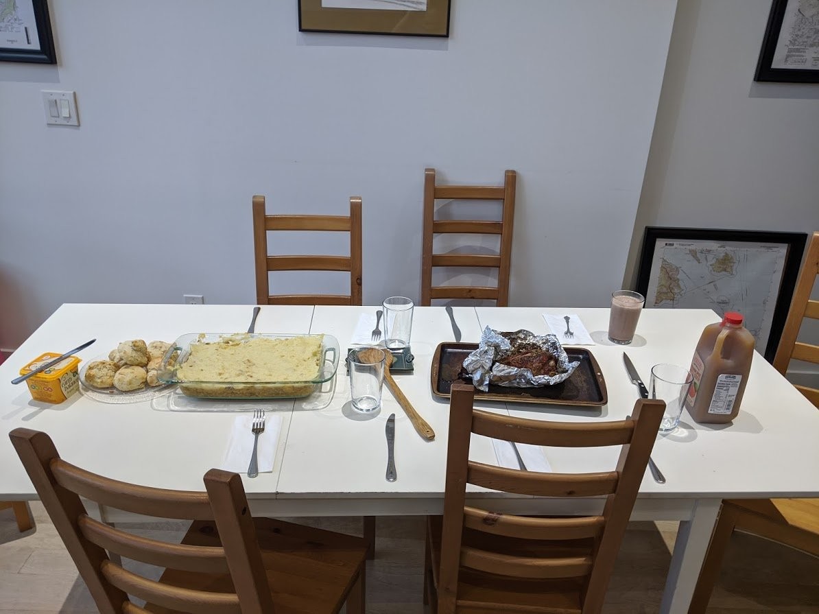 A table set with butter, a plate of biscuits, a casserole dish of shepherd's pie, and a giant single turkey leg