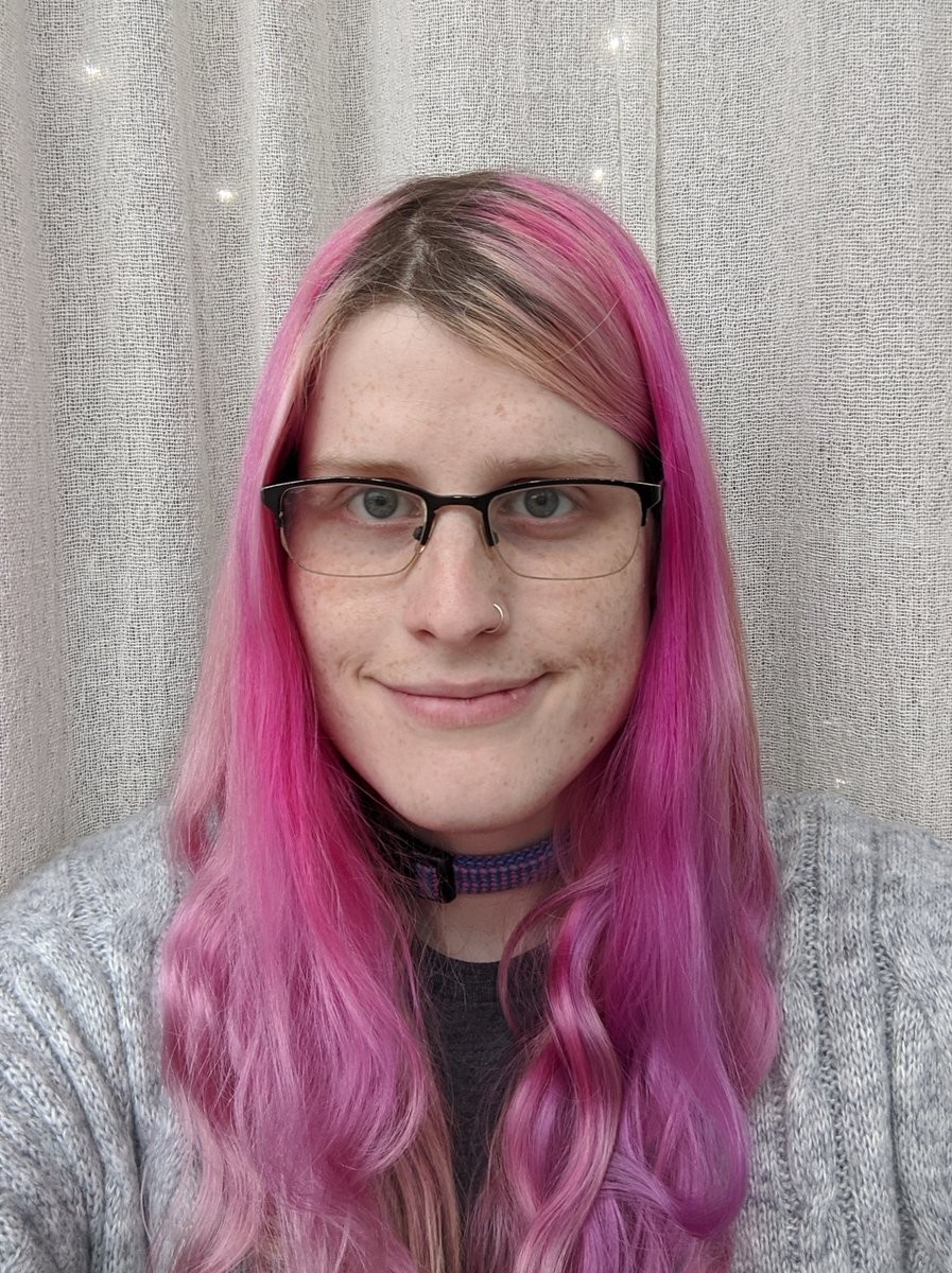 A woman with long pink hair in a cabled grey cardigan