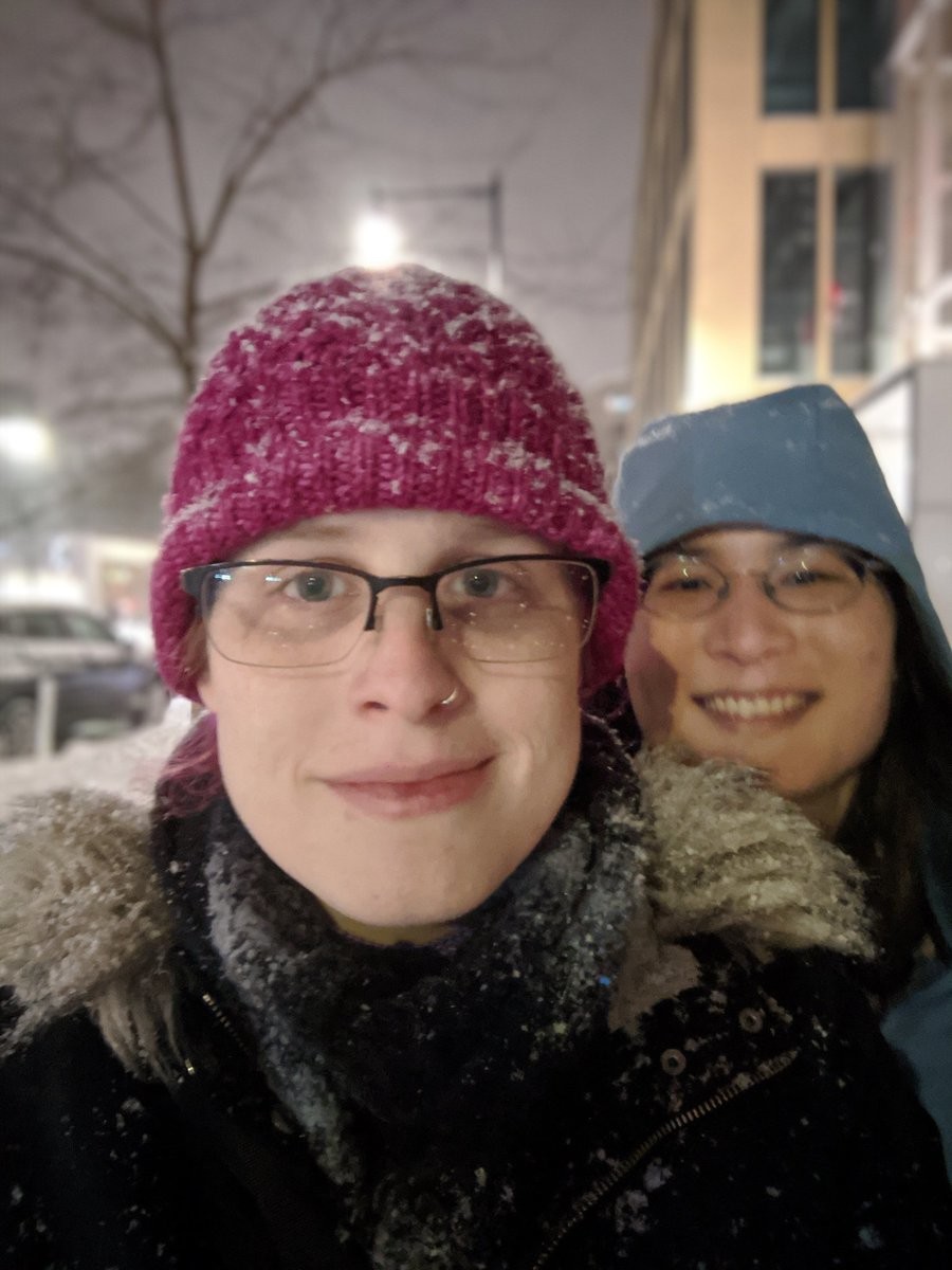 a selfie of me, pink hat covered in snow, with a smiling liz behind me