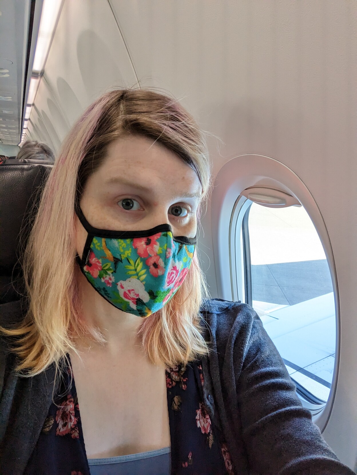 A woman in blind hair with brown roots and pink streaks on a plane